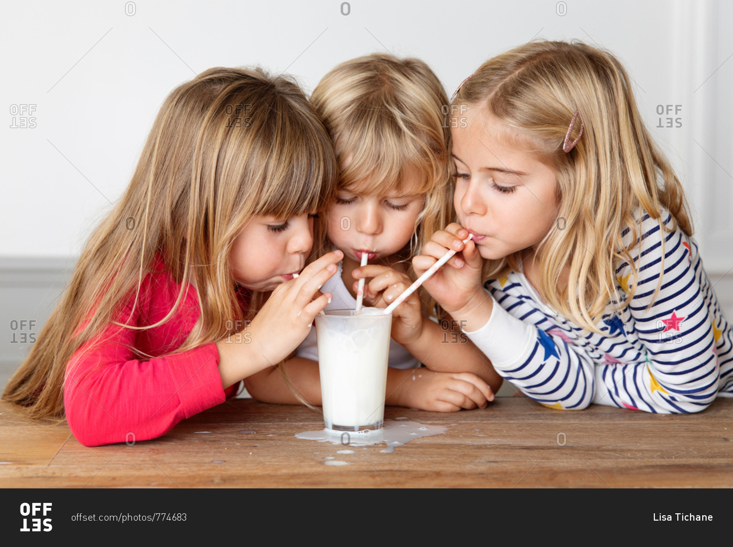 Three girls blowing bubbles in a glass of milk with drinking straws