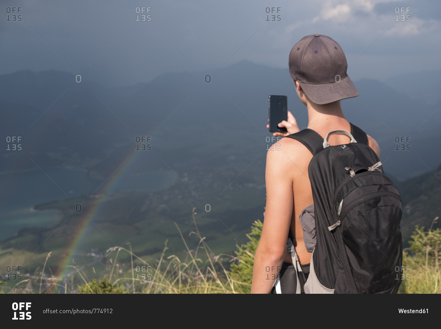Austria- Salzkammergut- Mondsee- teenage boy taking a scenic picture with rainbow
