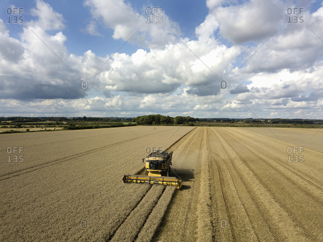 A drone shot of fields in a farming landscape, and a combine harvester working harvesting a crop.
