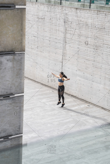Side view of young Latino woman in sportswear doing jumping jacks on walkway in Mexico city
