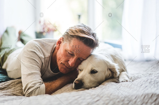 Retired man sleeping with dog comfortably on bed at home stock