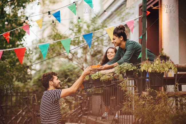 Smiling young woman giving food to male friend from balcony during garden party