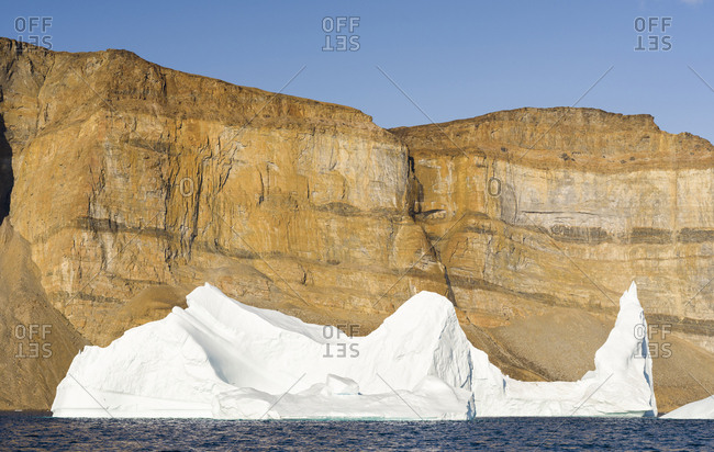 Landscape with steep yellow cliffs and icebergs in the Uummannaq fjord system, northwest Greenland.