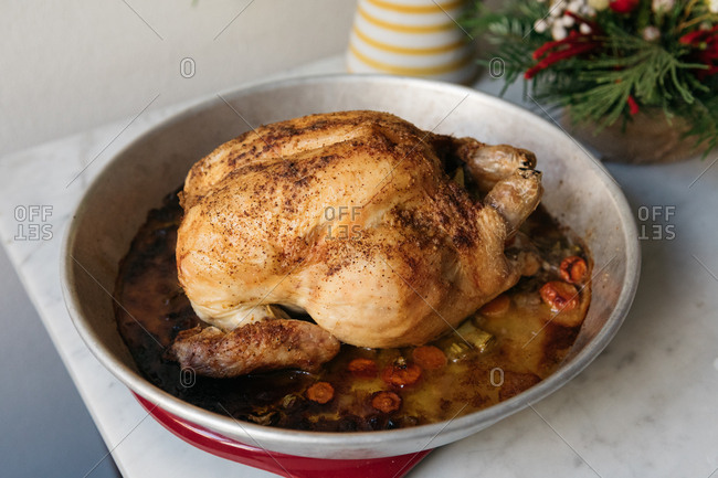 Whole roasted chicken cooked with vegetables in a serving dish