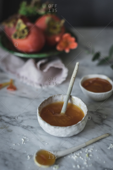 Small spoon lying in bowl with fresh honey for panna cotta on marble tabletop