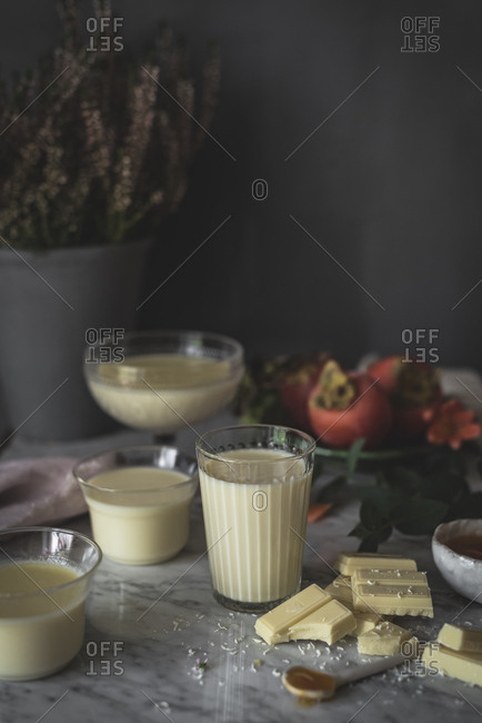 Pieces of yummy white chocolate lying on marble tabletop near containers with delectable panna cotta