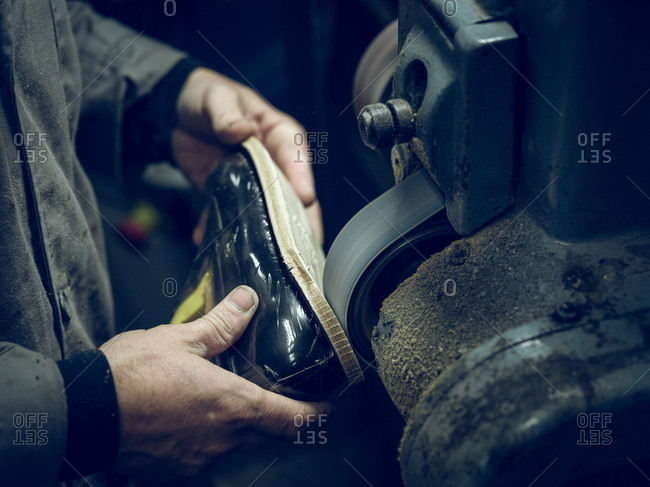 Unrecognizable man using polishing machine on sole of stylish footwear in workshop