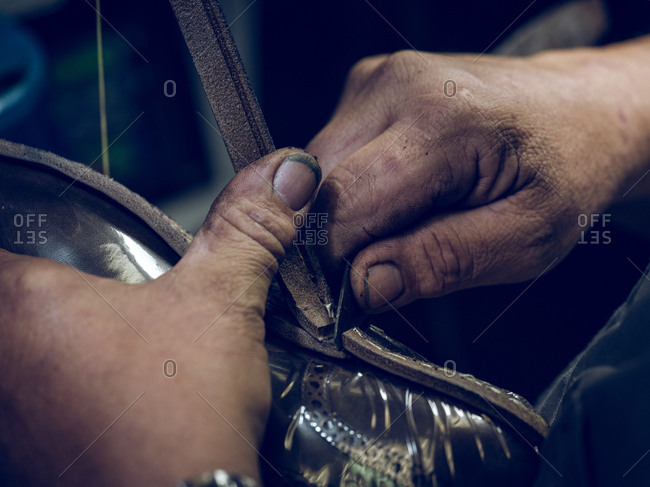 Closeup dirty hands of shoemaker cutting leather from shoes while working in workshop