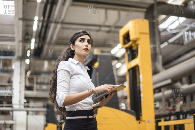 Woman with tablet in factory shop floor looking around