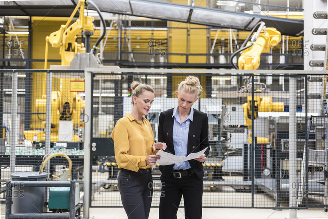 Two women discussing plan in factory shop floor with industrial robot