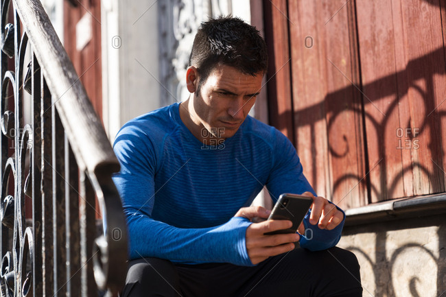 Athlete sitting on front stoop using cell phone
