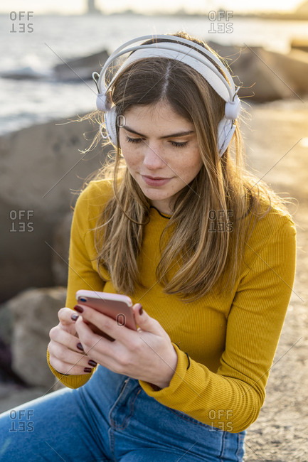 Young beautiful woman listening music with headphones and Smartphone by the sea