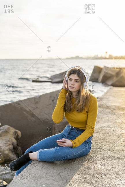 Young beautiful happy woman listening music with headphones by the sea