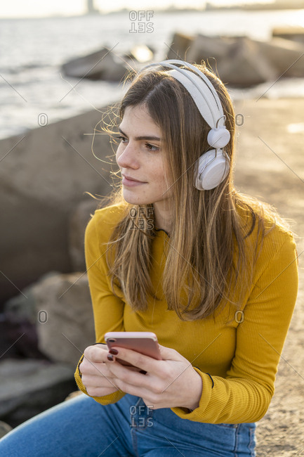 Young woman listening music with headphones and Smartphone by the sea