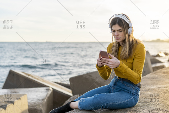 Beautiful young woman listening music with headphones and Smartphone by the sea
