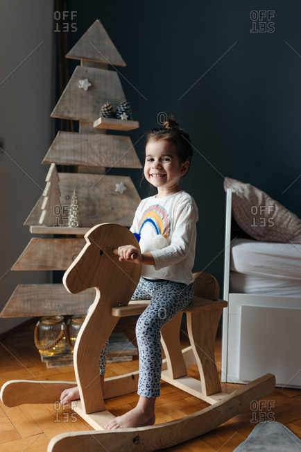 Girl sitting on her wooden horse in front of the wooden Christmas tree