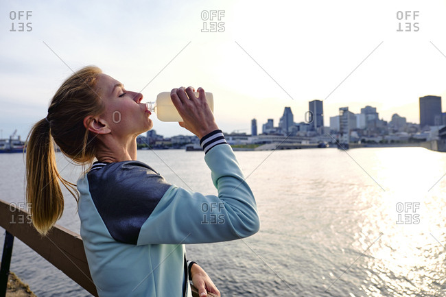 Woman drinking water with cityscape behind, Montreal, Quebec, Canada