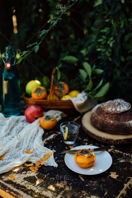 Peeled persimmon on a plate with a knife on a wooden table with a variety of fruit