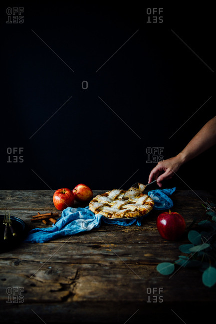 Person slicing into a whole apple pie with a pie server