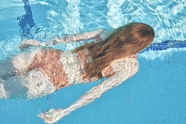 Young redheaded woman swimming underwater in a pool