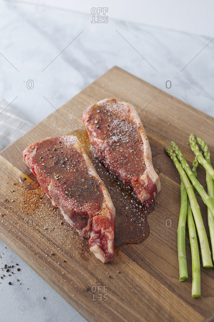 Overhead view of raw steaks are prepped on a cutting board for grilling