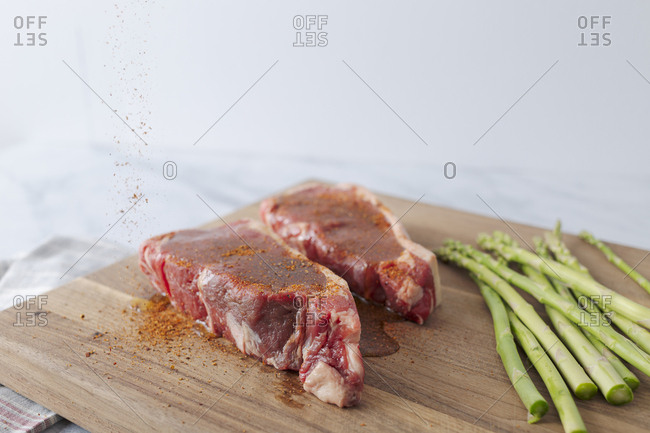 Two raw steaks are prepped on a cutting board for grilling