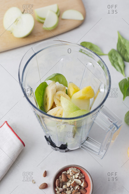 Fruit smoothie ingredients in blender beside nuts
