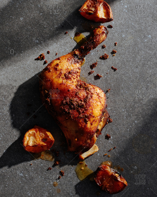 Paprika chicken that has been roasted with paprika and fennel seeds shown with blackened lemons on a concrete surface