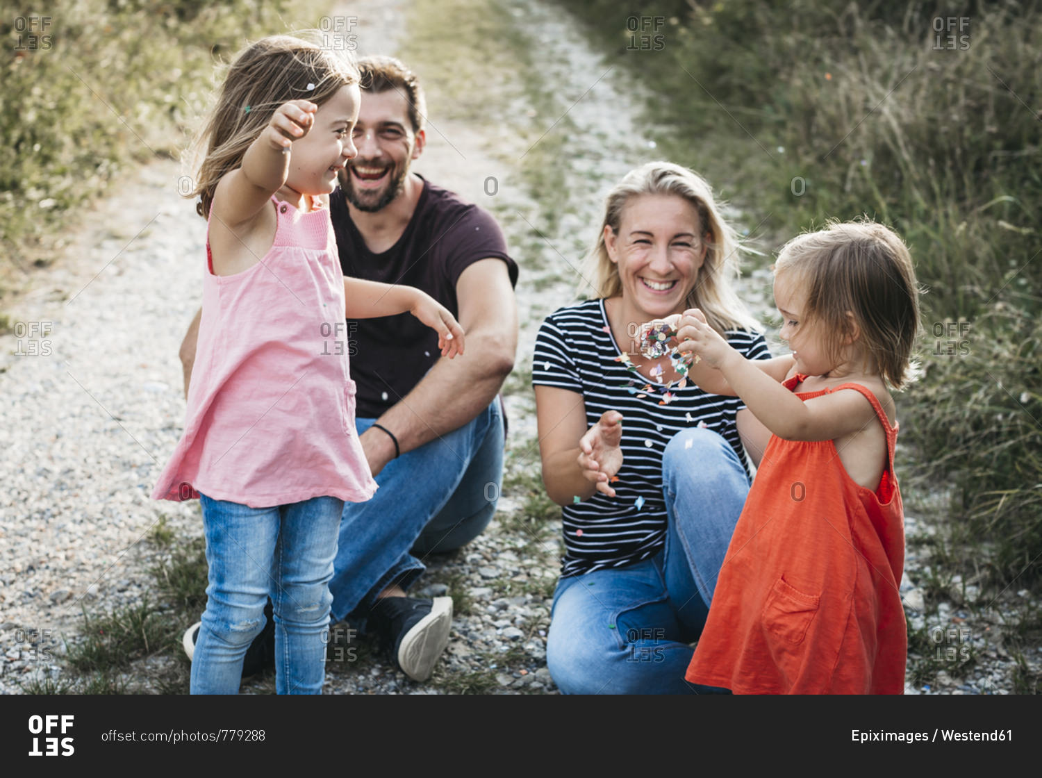 Happy family with two daughters playing with confetti on a field path