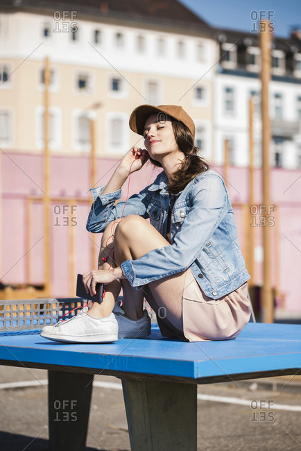 Relaxed young woman sitting on table tennis table listening to music