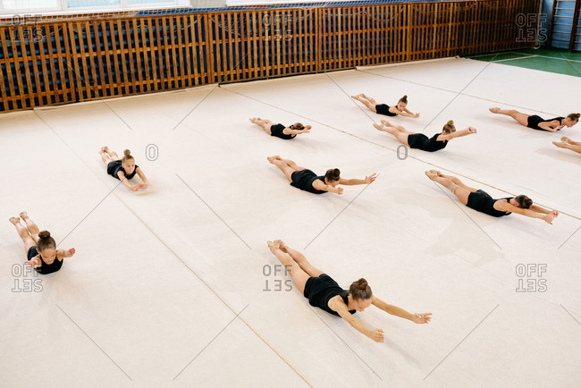 Group of gymnasts in black sports wear lying on the floor doing rhythmic gymnastics in sports hall