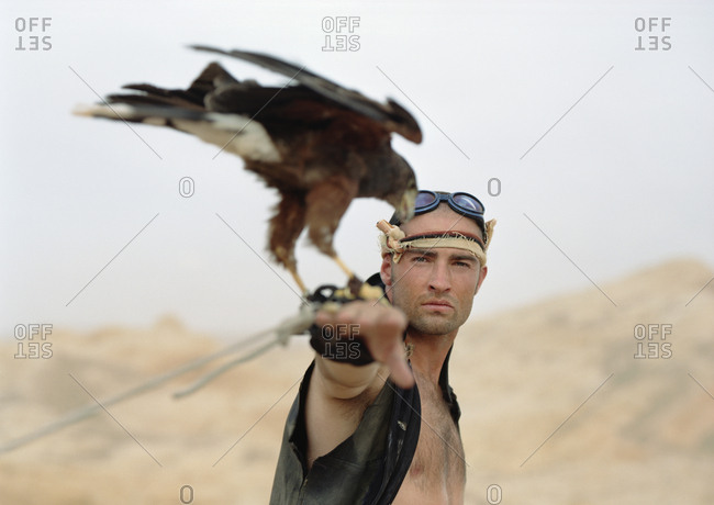 Portrait of a young man standing with a bird of prey perched on his wrist.