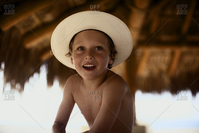 Portrait of a topless boy sitting under the thatched canopy.