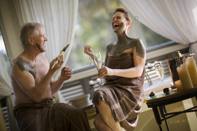 Mature couple laughing while covering each other in mud inside their bathroom.