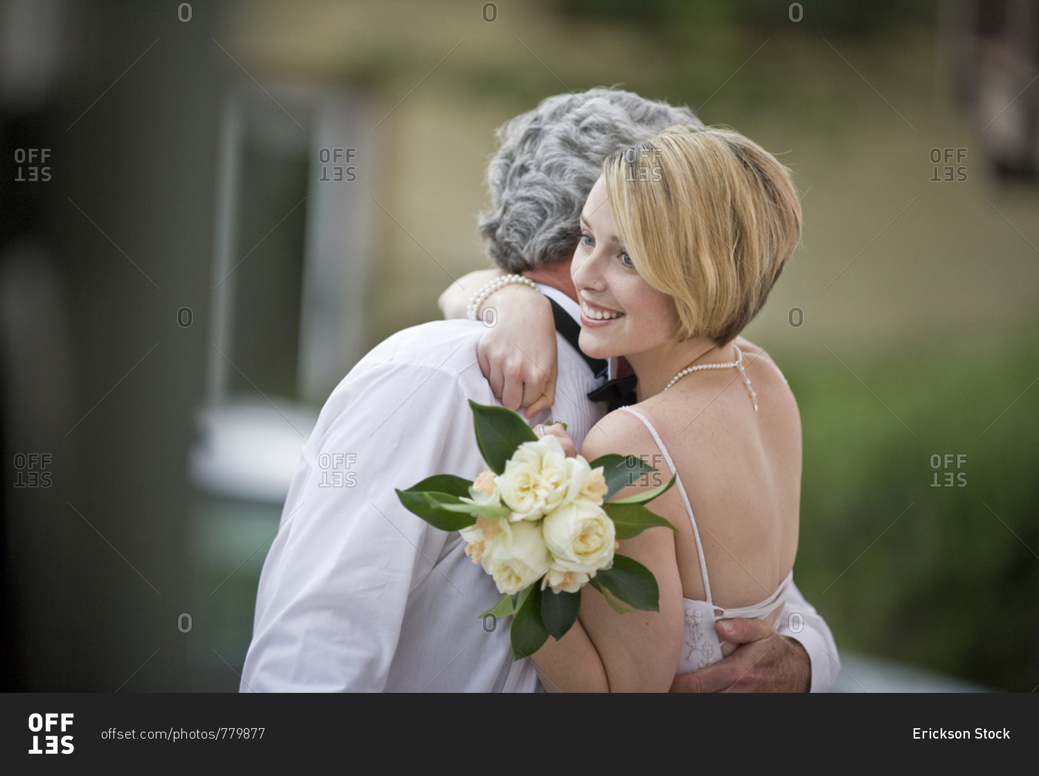 Smiling bride hugging the groom while holding a bouquet of roses.