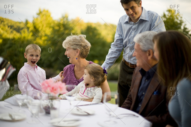 Multi-generational family sitting at an outside table of a restaurant watching a young boy be entertaining.