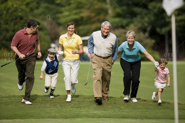 Portrait of a mature adult man running along a golf course with his extended family.