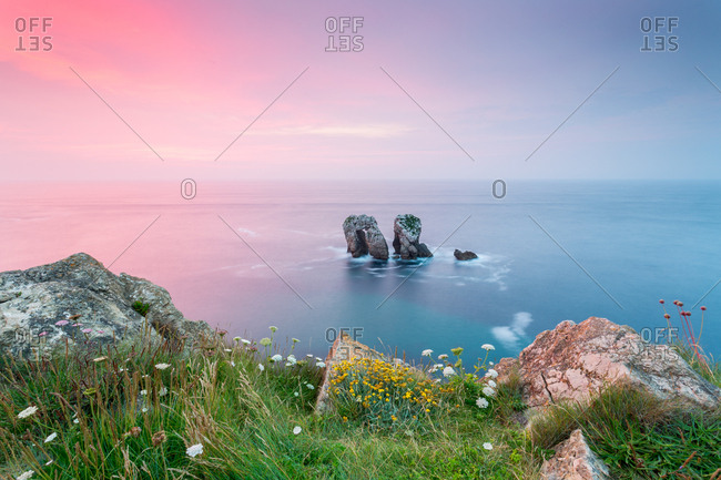Picturesque view of two rocks in middle of calm sea against blue and pink morning sky