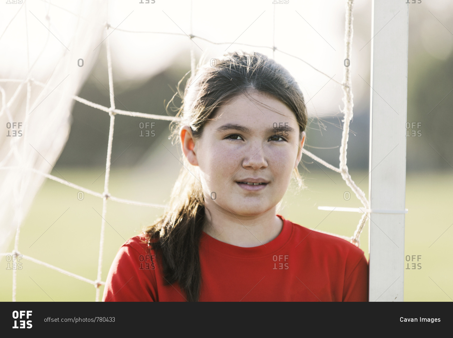 Portrait of confident soccer player wearing red uniform against goal post during sunny day