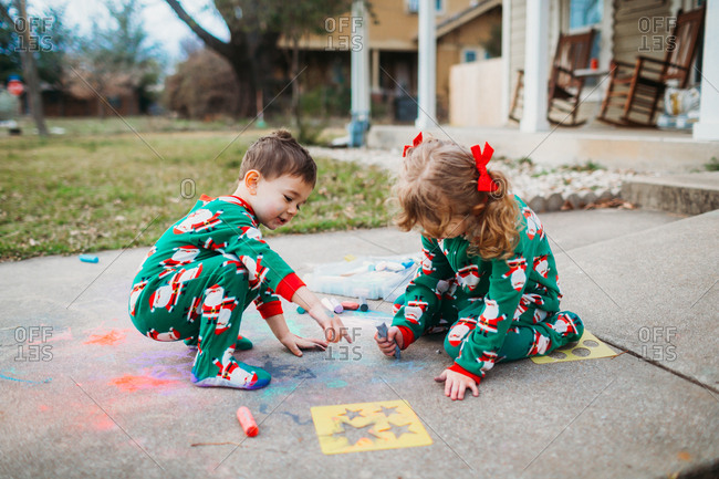 Young siblings drawing on sidewalk with chalk in Santa pajamas
