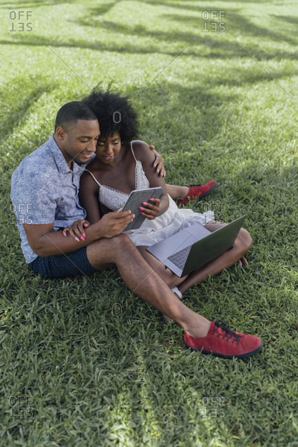 Smiling young couple sharing tablet on lawn in a park