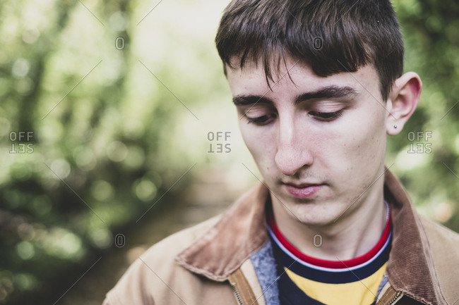Portrait of young man with short brown hair wearing brown jacket standing in forest.