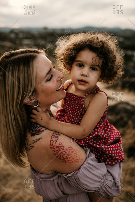 Mother with tattoos and stretched ears holding daughter in nature