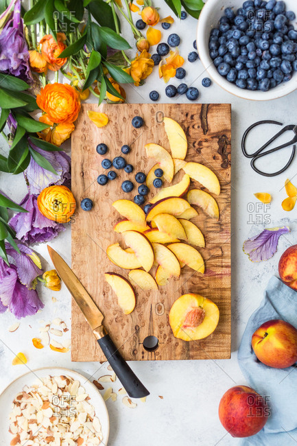 Blueberries and peaches being cut on a cutting board by almonds and flowers