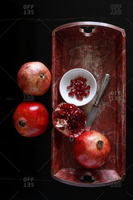 Whole pomegranate and pomegranate seed with bowl and knife on wooden tray
