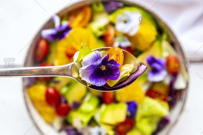 Spoon of mixed salad with avocado- tomatoes and edible flower- close-up