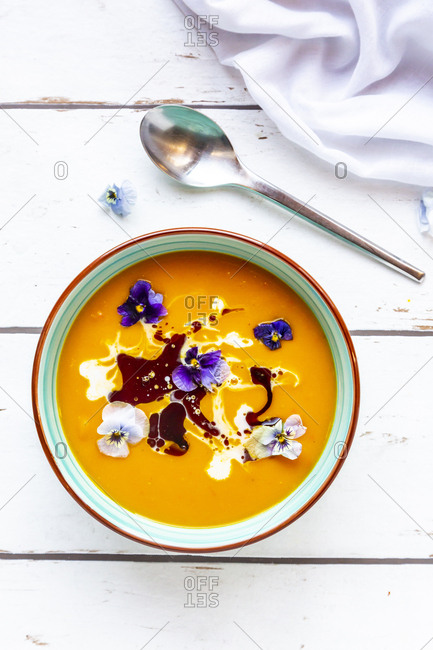 Bowl of creamed pumpkin soup garnished with edible flowers