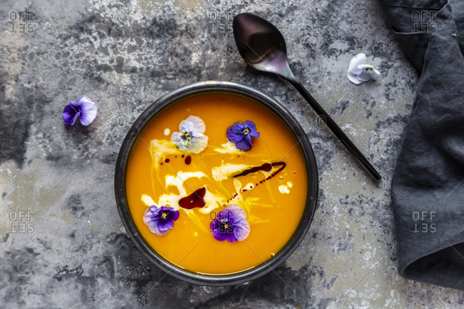 Bowl of creamed pumpkin soup garnished with edible flowers