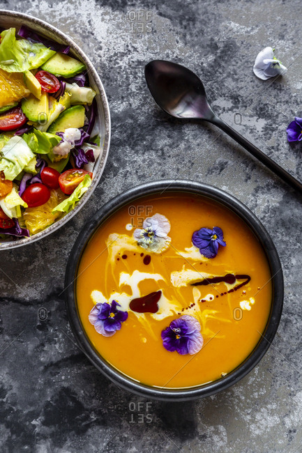 Bowl of mixed salad with edible flowers and bowl of creamed pumpkin soup garnished with edible flowers