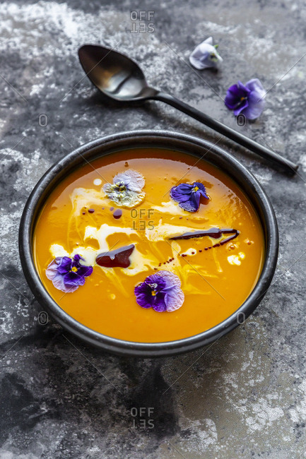 Bowl of creamed pumpkin soup garnished with edible flowers